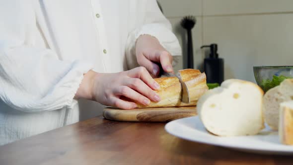 Woman Slicing Baguette at Chopping Board with Kitchen Knife Indoors