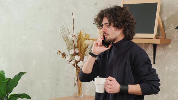 Man on Kitchen is Smiling Drinking Coffee and Talking on a Smart Phone