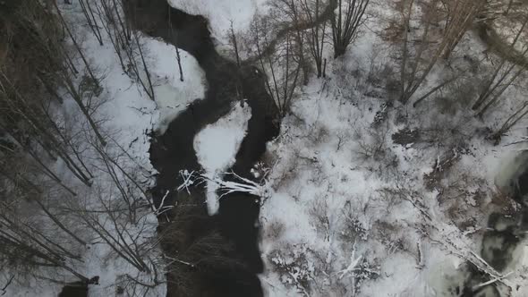 Aerial tilt-up reveal of small river in snowy woods. Latvia