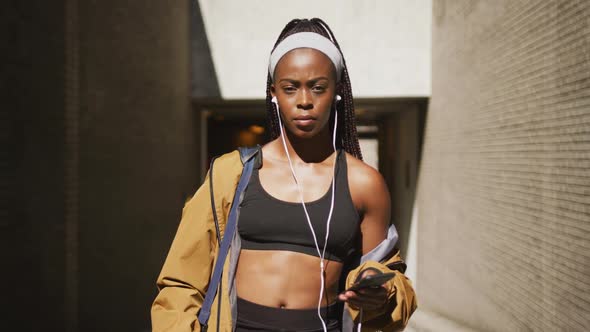 Portrait of african american woman exercising outdoors wearing earphones and smiling to camera