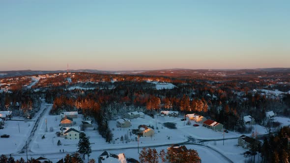 Scenic sunset aerial flying over a snowy residential subdivision on a cold, winter evening.