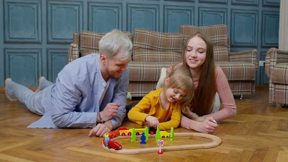 Young Mother and Father Playing with Child Daughter Riding Toy Train on Wooden Railroad Game at Home