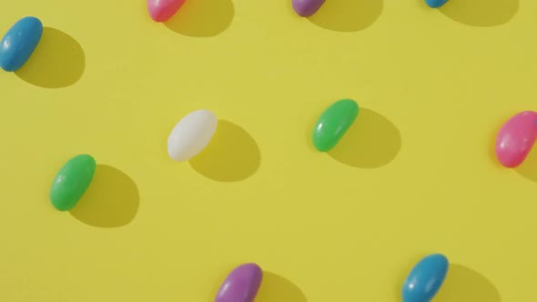Video of overhead view of rows of multi coloured sweets over yellow background