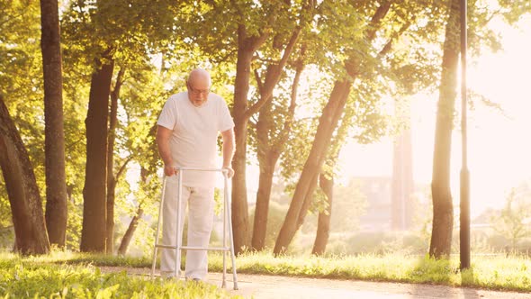 Disabled old man is walking with a walker. Handicapped patient in the park.
