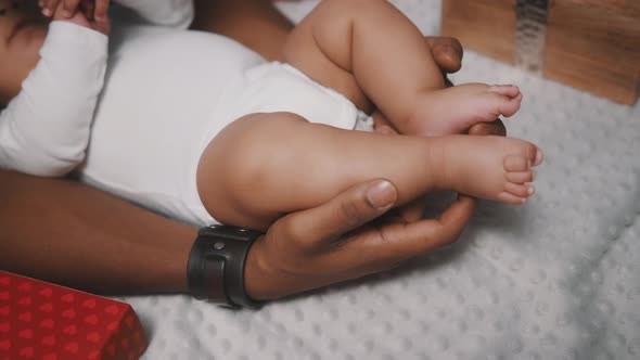 Cute Baby Feet in the Hands of Black Father Surrounded By Christmas Gifts Close Up