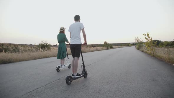 Happy Couple Riding on Electric Scooters Into the Distance and Having Fun on Way