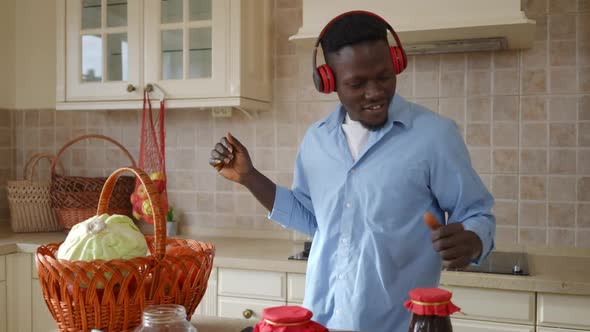 Joyful Satisfied African American Young Man in Headphones Dancing in Kitchen at Home Indoors