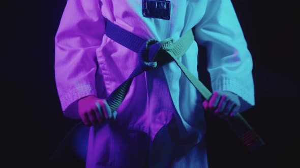 A Little Boy Doing Taekwondo in Neon Lighting  Tying Up His Green Belt on the Waist