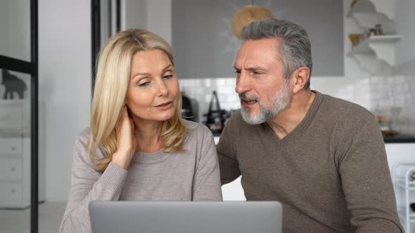 Cheerful Middleaged Couple with a Laptop Sitting at the Desk in Modern Kitchen at Home