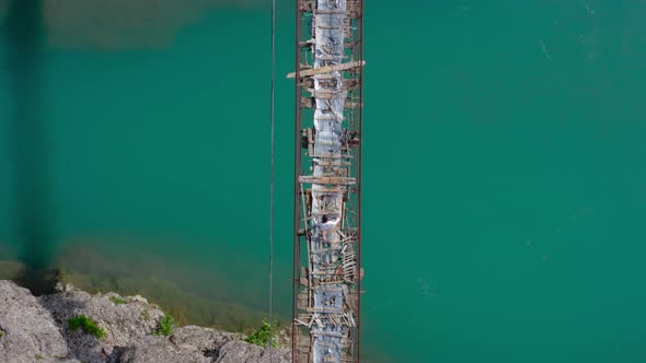 Aerial top down of solo traveler balancing and walking on rickety wooden bridge over river.