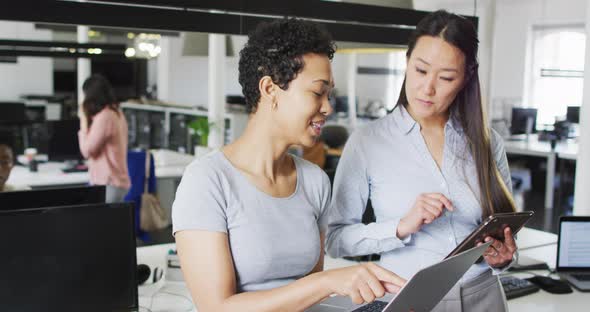 Focused diverse businesswomen working together on laptop and tablet in office