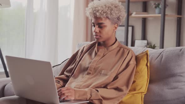 Focused African Woman Typing on Laptop Browsing Internet Using Apps Sit on Sofa