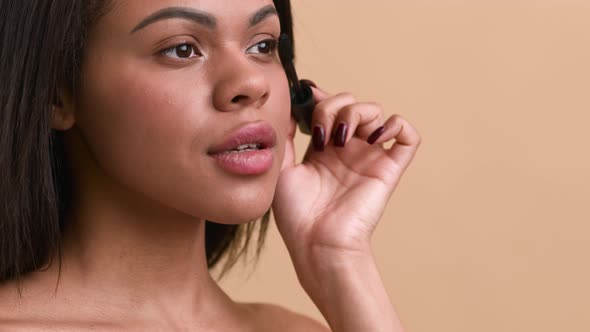 Black Female Applying Mascara On Eyelashes Making Makeup Beige Background