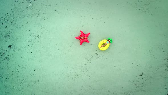 Aerial view of two girls floating on inflatable mattress in transparent sea.