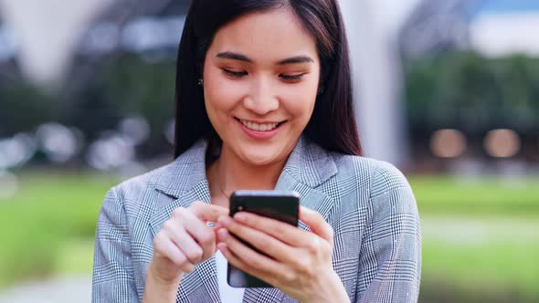 young asian woman is looking down at her mobile phone happily