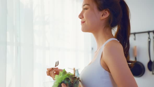 Asian attractive sport woman holding salad bowl and eat vegetables.