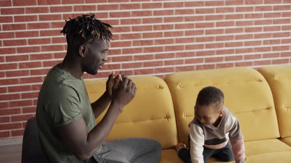 Affectionate African Father Tickling Little Adorable Child Son Having Fun Laughing Relaxing on Sofa