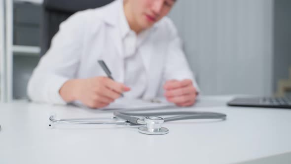 Close up of Asian male doctor write note on table in office hospital.