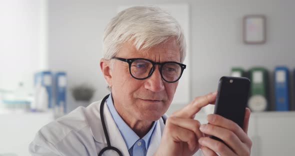 Senior Male Doctor Using Mobile Phone Technology Apps at Desk