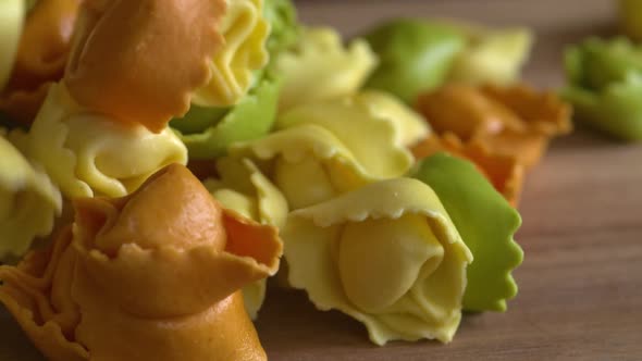 A bunch of fresh, rainbow tortellini dropping into a pile on a wood cutting board