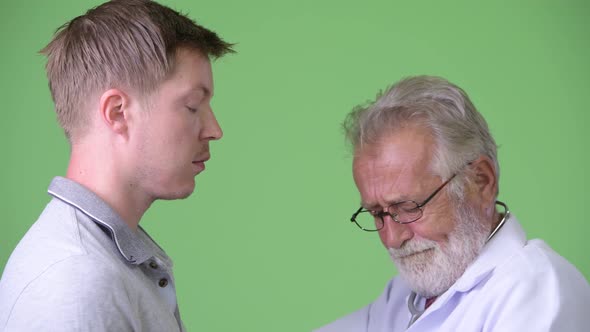 Senior Bearded Man Doctor Consulting Man Patient Against Green Background