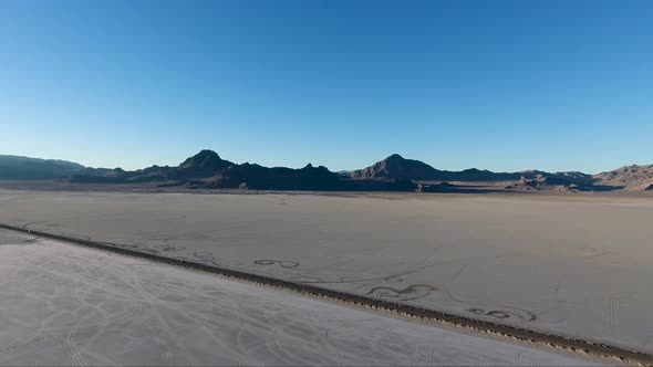 Car tracks in the salt and  a car driving across the Bonneville Salt Flats causeway are seen from ab