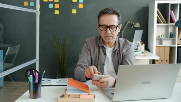 Mature Employee Calling on Mobile Phone and Using Laptop Computer in Office