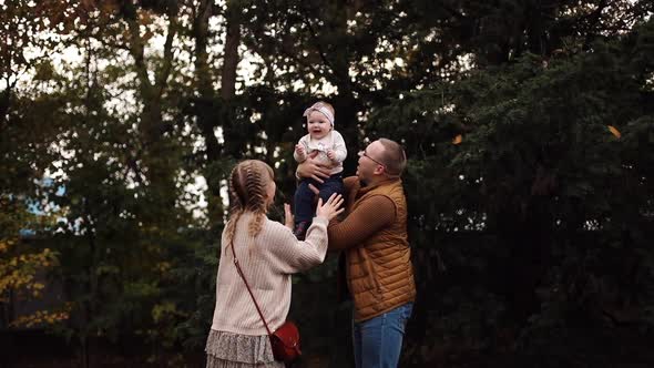 Loving Mother Kissing Her Daughter on Father's Hands in Park.