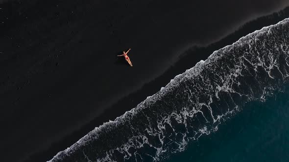 Top View of a Girl in a Red Swimsuit Lying on a Black Beach on the Surf Line. Coast of the Island of