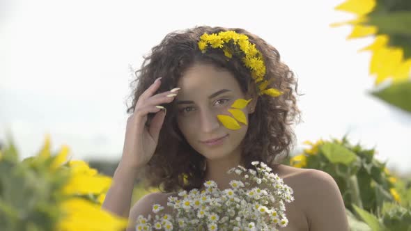 Portrait of a Beautiful Curly Girl Looking at the Camera Touching Her Hair Standing on the Sunflower
