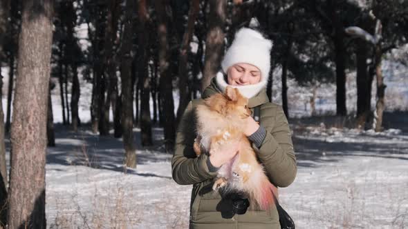 Cute Young Girl Holds Pet Dog of the Spitz Breed in Her Arms in Winter Forest