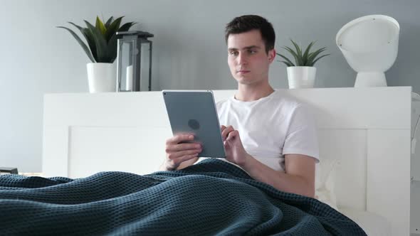 Man Using Tablet While Lying in Bed