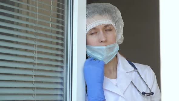 Tired Woman Doctor in Protective Suit Looks Out Window, Takes Off His Medical Mask, Closing His Eyes