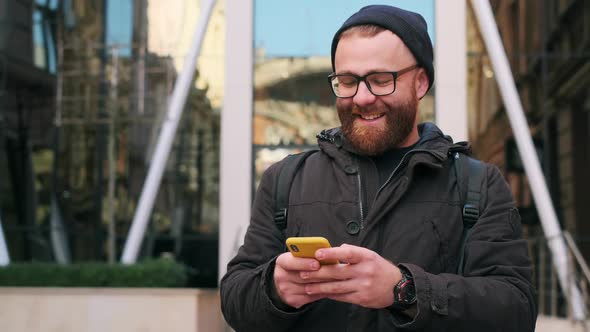 Bearded Man in Glasses Typing Message and Laughing While Looking at Screen and Aside, Handsome Guy