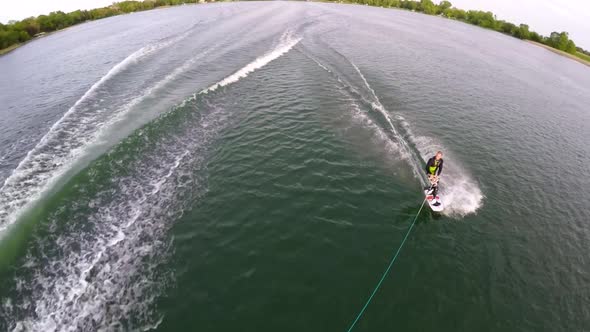 Aerial birds-eye drone view of a man wakeboarding behind a boat.