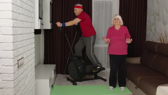 Senior Elderly Couple Using Orbitrek Doing Workout Weight Lifting Sport Dumbbells Exercises at Home