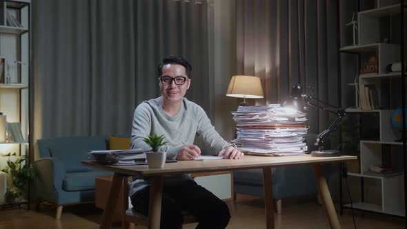 Asian Man Smiling To Camera While Working With Documents At Home