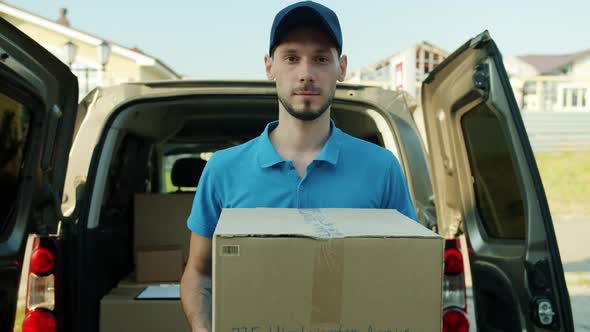 Portrait of Deliveryman in Uniform Holding Carton Box Standing Outside Near Van with Packages