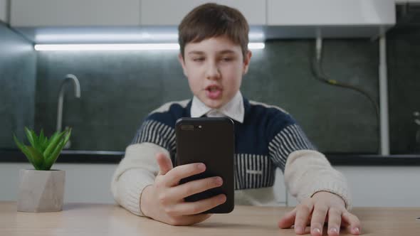 13 Years Old Boy Making Video Call Using Smartphone While Sitting at Table at Home Kitchen