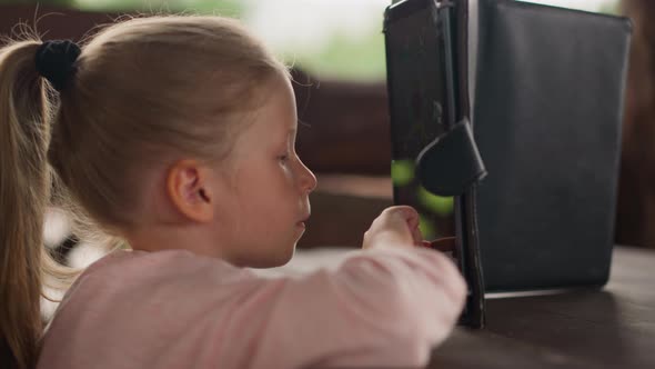 Tranquil Little Child Plays on Tablet PC at Table in Cafe