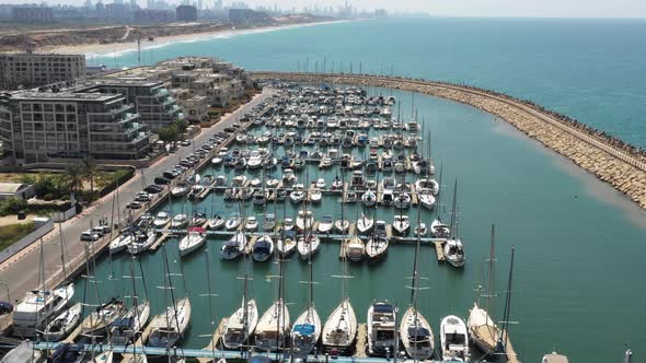 Several sailboats and luxury motor yachts are moored on the long piers with luxury apartments right