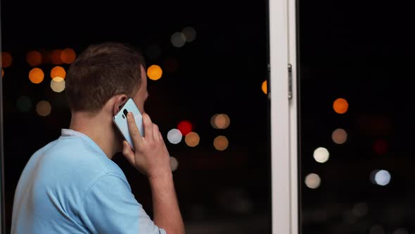 A Man Talking on the Phone Standing at the Open Window at Night Rear View