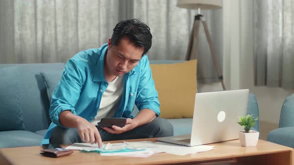 Asian Man With A Laptop Holding Bill And Calculator To Calculate Money At Home