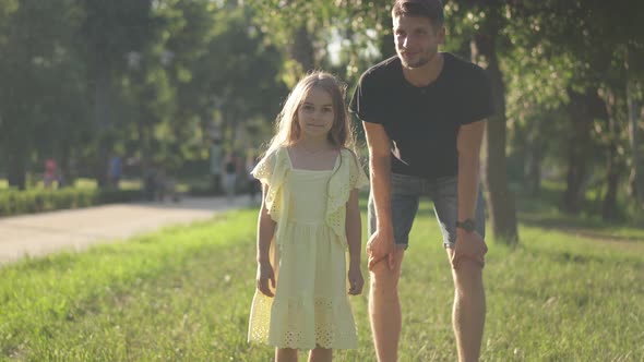 Dolly Shot of Cheerful Cute Girl with Father in Sunny Park Running Looking at Camera Leaving