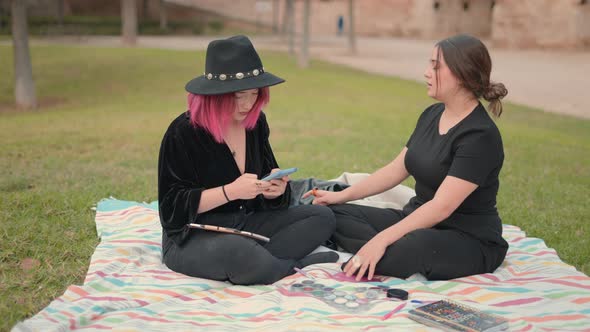 Attractive White Girls Sitting on Sheet on the Grass in the Park