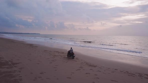 Drone view of a motorcycle riding on the beach side during sunset