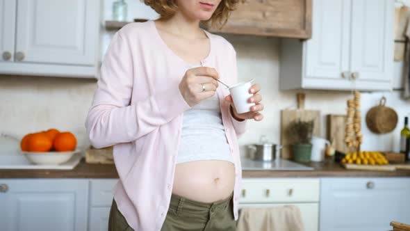 Young Pregnant Woman Eating Yogurt In The Kitchen