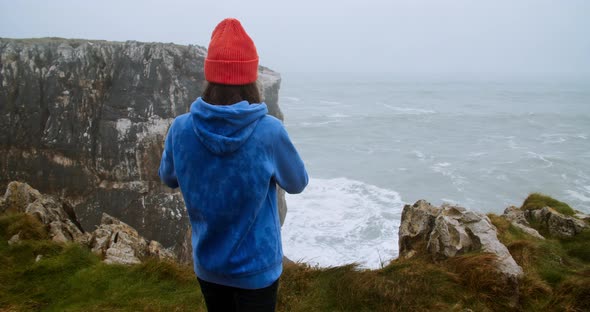 Female Traveler Shoot Ocean Storm Waves Using Smart Phone Stand on Edge of Cliff