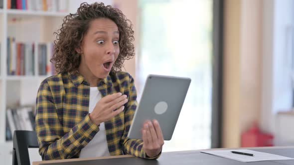 Winning Young Mixed Race Woman Celebrating Success on Tablet