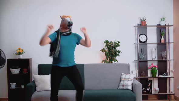 In the room, a man dances in a horse mask, spreading his arms to the sides